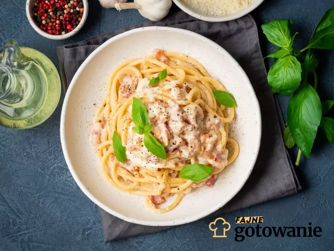 Pyszne spaghetti carbonara ze śmietaną bez jajek, udekorowane bazylią i pieprzem. Obok butelka oliwy i miseczka z pieprzem.