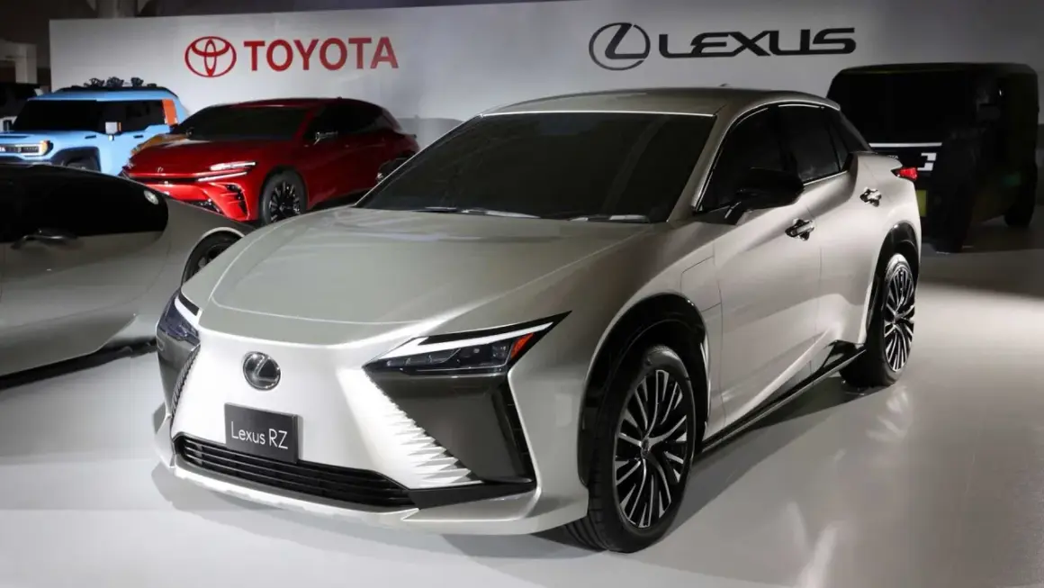 Elegancki, srebrny Lexus RZ prezentuje się na tle logo Toyoty i Lexusa.