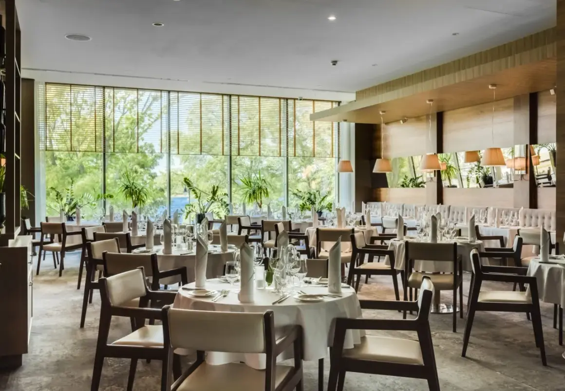 Elegancka sala restauracyjna Grand Hotel Tiffi w Iławie, z widokiem na zieleń. Stoły nakryte do posiłku, gotowe na przyjęcie gości.