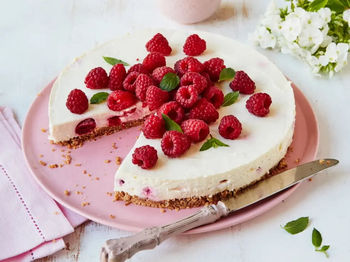 Eine köstliche Philadelphia Torte Himbeer, üppig garniert mit frischen Himbeeren und Minze, auf einem rosa Teller.