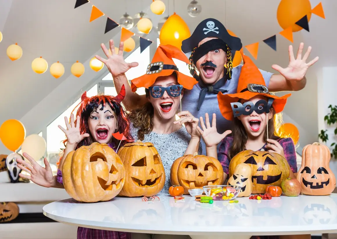 Famille costumée, joyeuse, prête à organiser soirée d'Halloween avec citrouilles sculptées et bonbons.