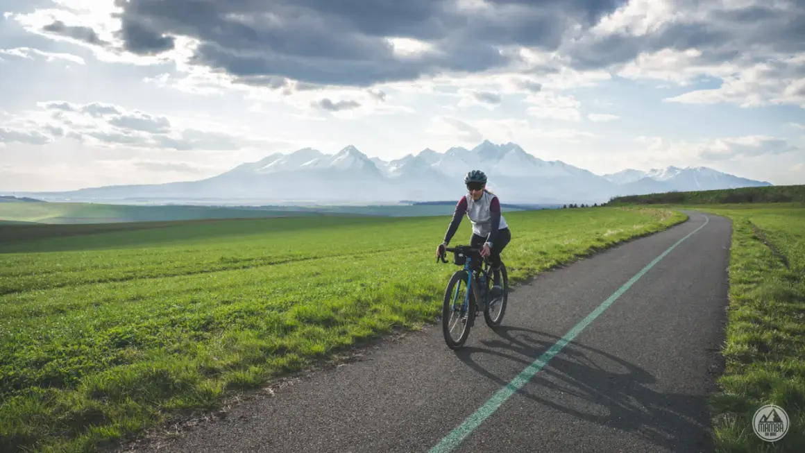 Kobieta na rowerze przemierza malowniczą trasę z widokiem na ośnieżone Tatry. To idealne miejsce na **velo tatry** i podziwianie krajobrazów.