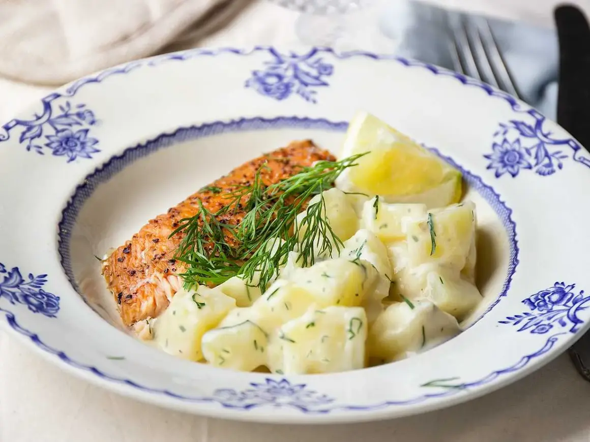 En bit stekt lax med citron och en generös portion krämig dillstuvad potatis på en vacker blåvit tallrik.