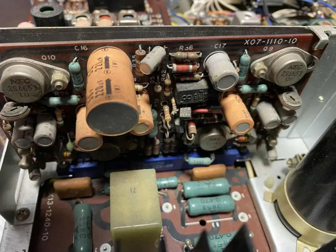 Wnętrze starego urządzenia elektronicznego z widocznymi kondensatorami, rezystorami i tranzystorami. Jeden z kondensatorów ma oznaczenie 220uF, a obok niego widać potencjalny problem z dc offset.