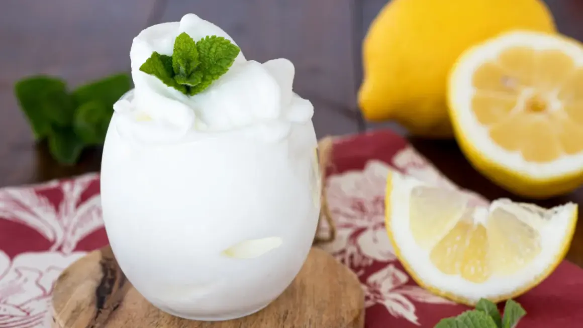 Sorbetto al limone fatto in casa, fresco e profumato, guarnito con menta. Accanto, limoni freschi e una tovaglietta rossa.
