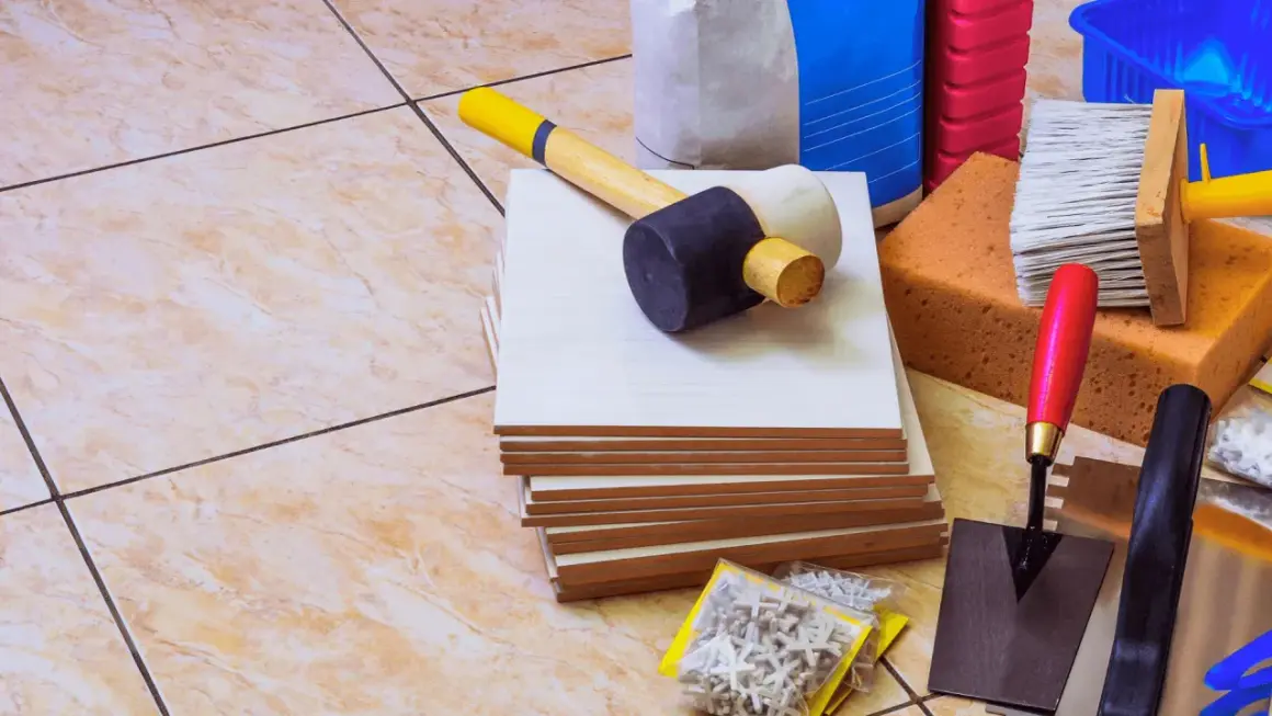 Outils pour coller du carrelage avec du ciment : carreaux, maillet, truelle, éponges, brosse, croisillons et sacs de ciment.