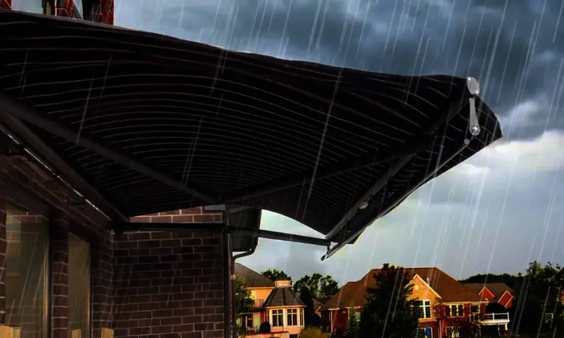 A dark, striped awning installation provides shelter from a heavy rain shower over a brick house.