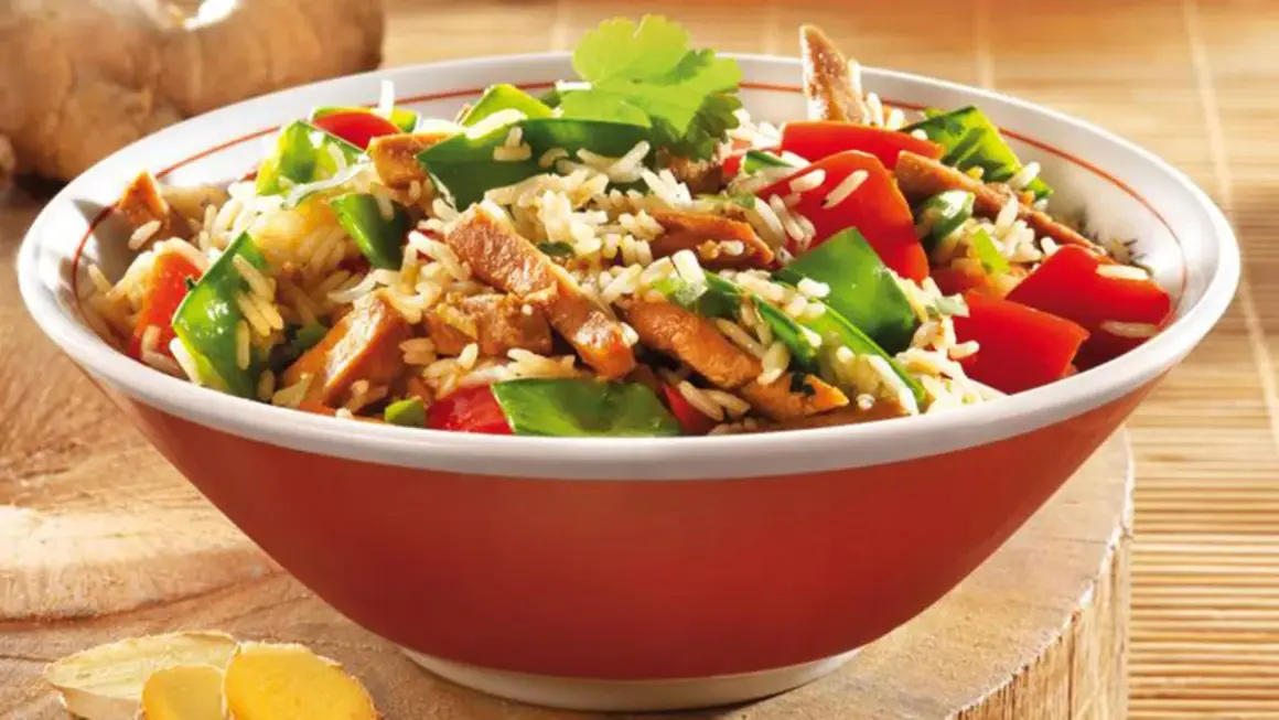 Schüssel mit Reis, Fleischstreifen, Paprika und Erbsen. Ein köstliches Gericht aus der Wok-Küche, garniert mit Koriander.