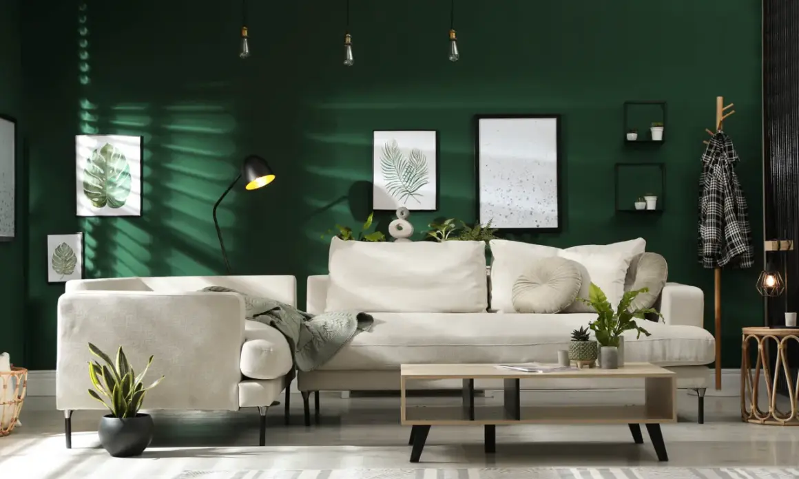 Ein gemütliches Wohnzimmer mit beiger Couch, Kaffeetisch und Pflanzen vor einer dunkelgrünen Wand. Ein Kleiderständer mit kariertem Mantel und ein trendiger Wandbehang vervollständigen das Bild.