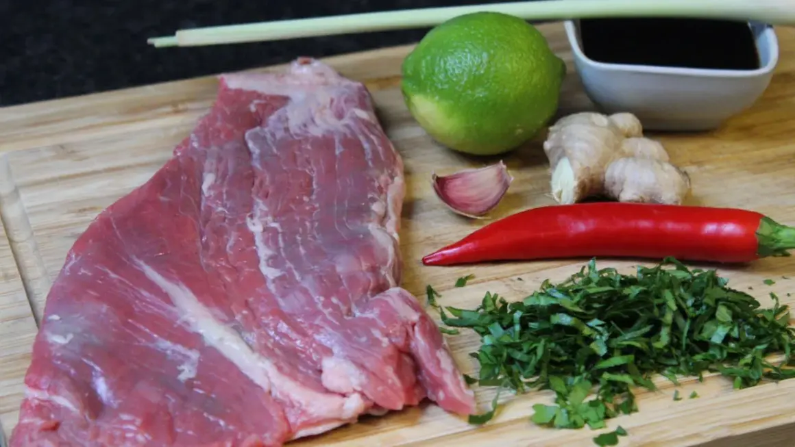 Rohes Rindersteak liegt bereit, um mit Limette, Ingwer, Chili, Knoblauch und Kräutern mariniert zu werden.