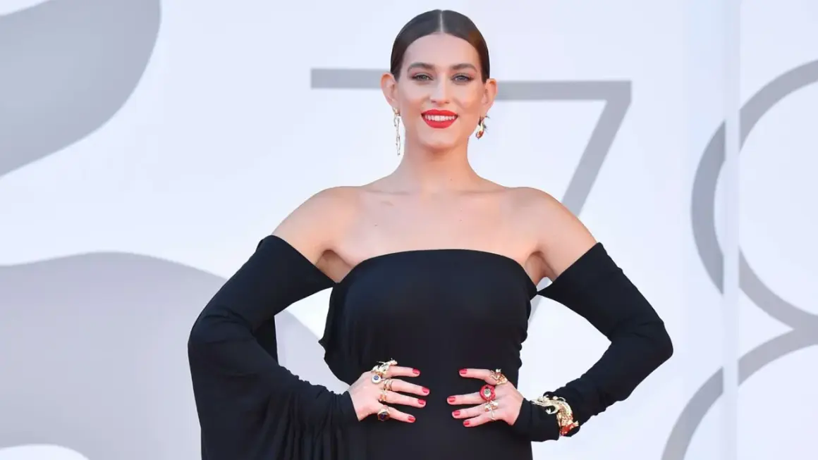 Gaia, la cantante, posa con un abito nero elegante e gioielli vistosi.