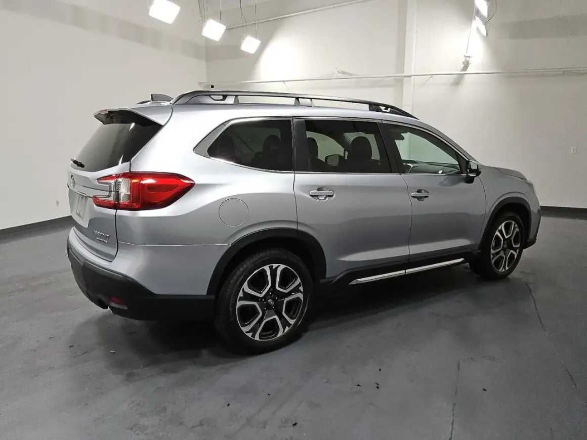 Srebrny Subaru Ascent z relingami dachowymi i przyciemnianymi szybami stoi na ciemnej podłodze.