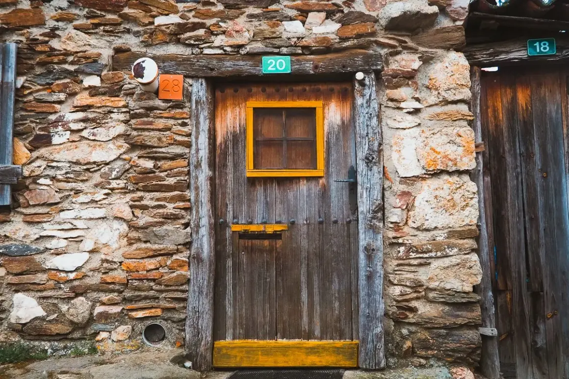 Puerta de madera rústica en una pared de piedra en la serrada de la fuente. Números 20, 28 y 18 adornan la entrada.