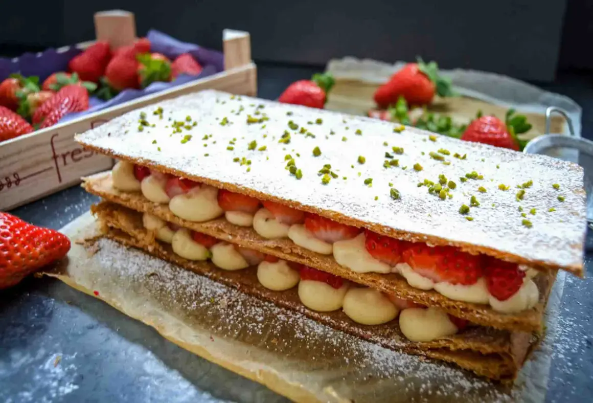 Ein köstliches Mille-feuille mit frischen Erdbeeren und Sahne, bestreut mit Puderzucker und Pistazien.