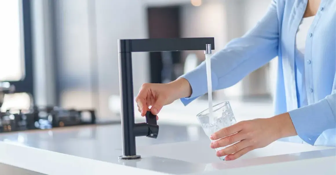 Une personne remplit un verre d'eau du robinet, peut-être pour tester la dureté de l'eau.