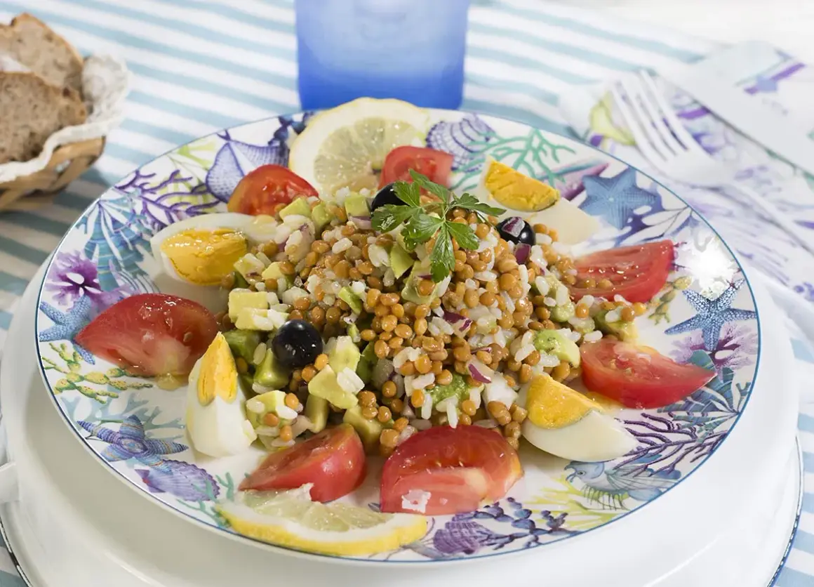 Deliciosa ensalada de lentejas y arroz con huevo duro, tomate, aguacate y aceitunas, servida en un plato con motivos marinos.