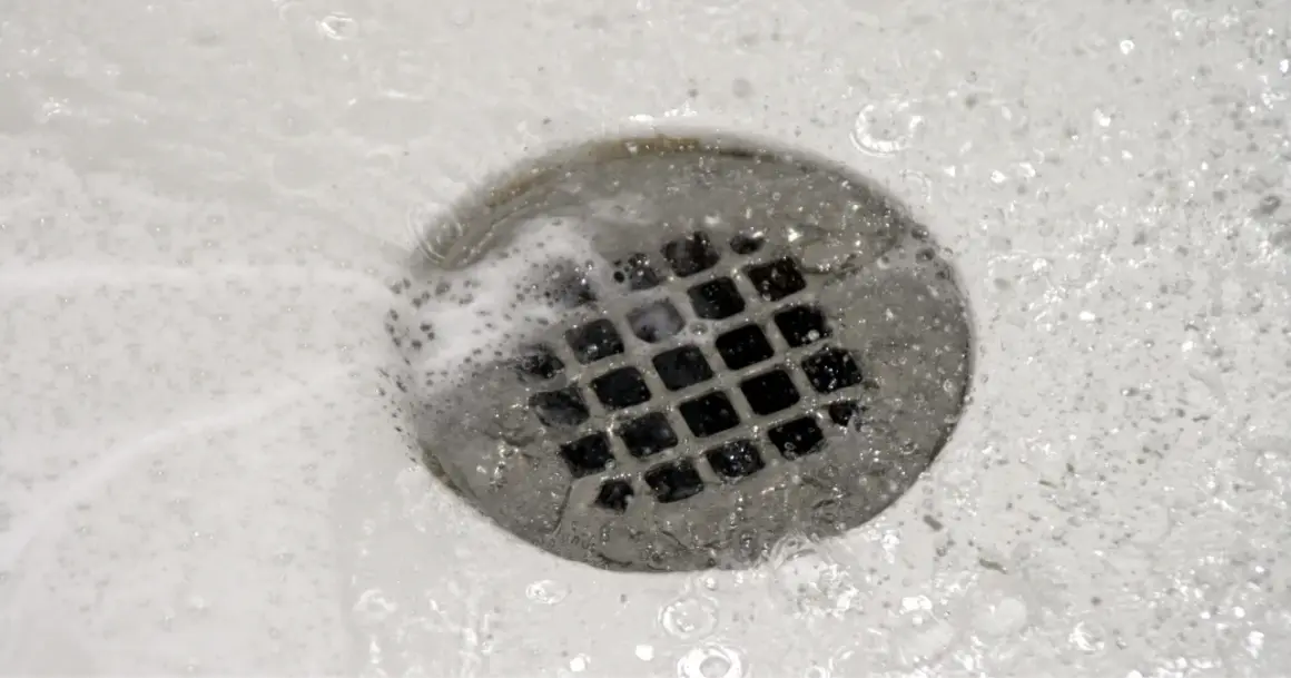Acqua e schiuma scorrono nello scarico della doccia, un segno che il lavoro di pulire scarico doccia è stato fatto.
