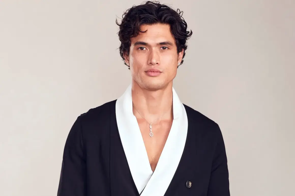 Charles Melton bär en svart kavaj med vit krage och ett diamant-halsband.
