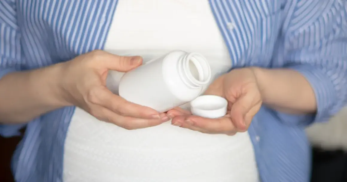 Kobieta w ciąży trzyma białą buteleczkę i jej nakrętkę. Rozważa, czy wziąć paracetamol w ciąży.