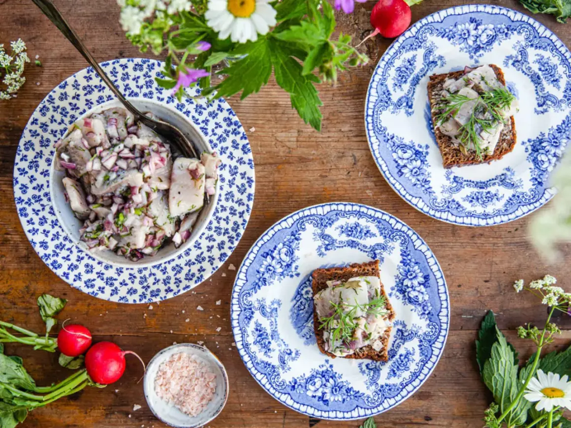 Brantevikssill recept på en vacker blåvit tallrik, med sill, rödlök och dill. Serveras på mörkt bröd.