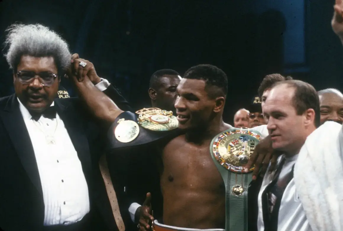 Don King raises Mike Tyson's arm, showcasing championship belts. A triumphant moment for the boxer and his promoter.