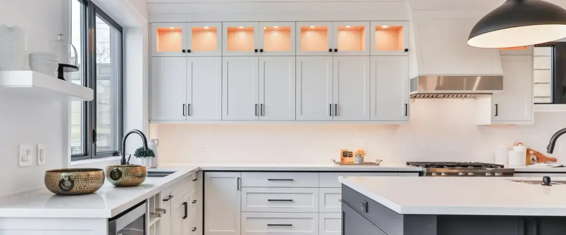Elegante cocina moderna con gabinetes blancos, encimeras de cuarzo y detalles dorados. La iluminación cálida realza la decoración de cocinas.