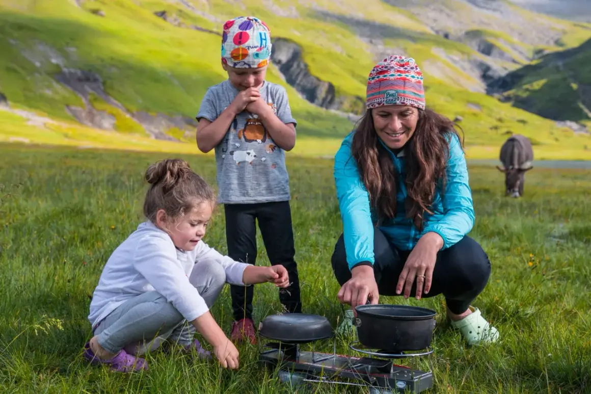 Une famille profite d'une micro aventure en famille dans un paysage montagneux verdoyant, préparant un repas en plein air.