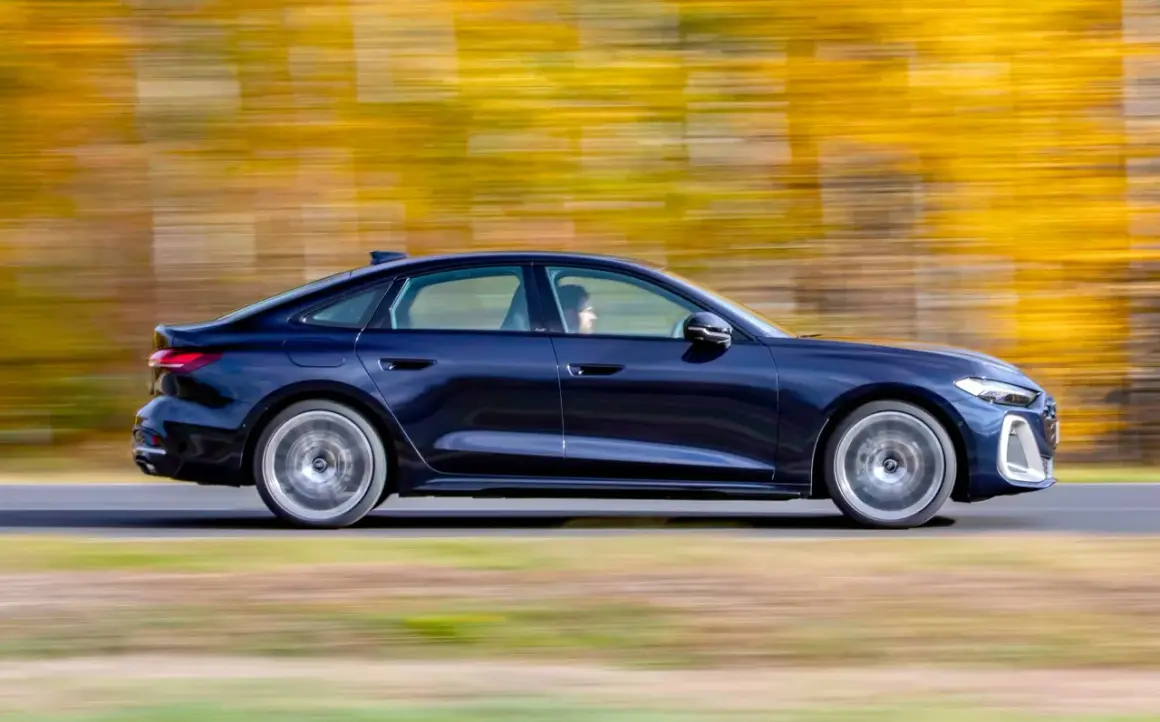 Ciemnoniebieskie Audi A4 B10 w ruchu, z rozmytym tłem jesiennych drzew.