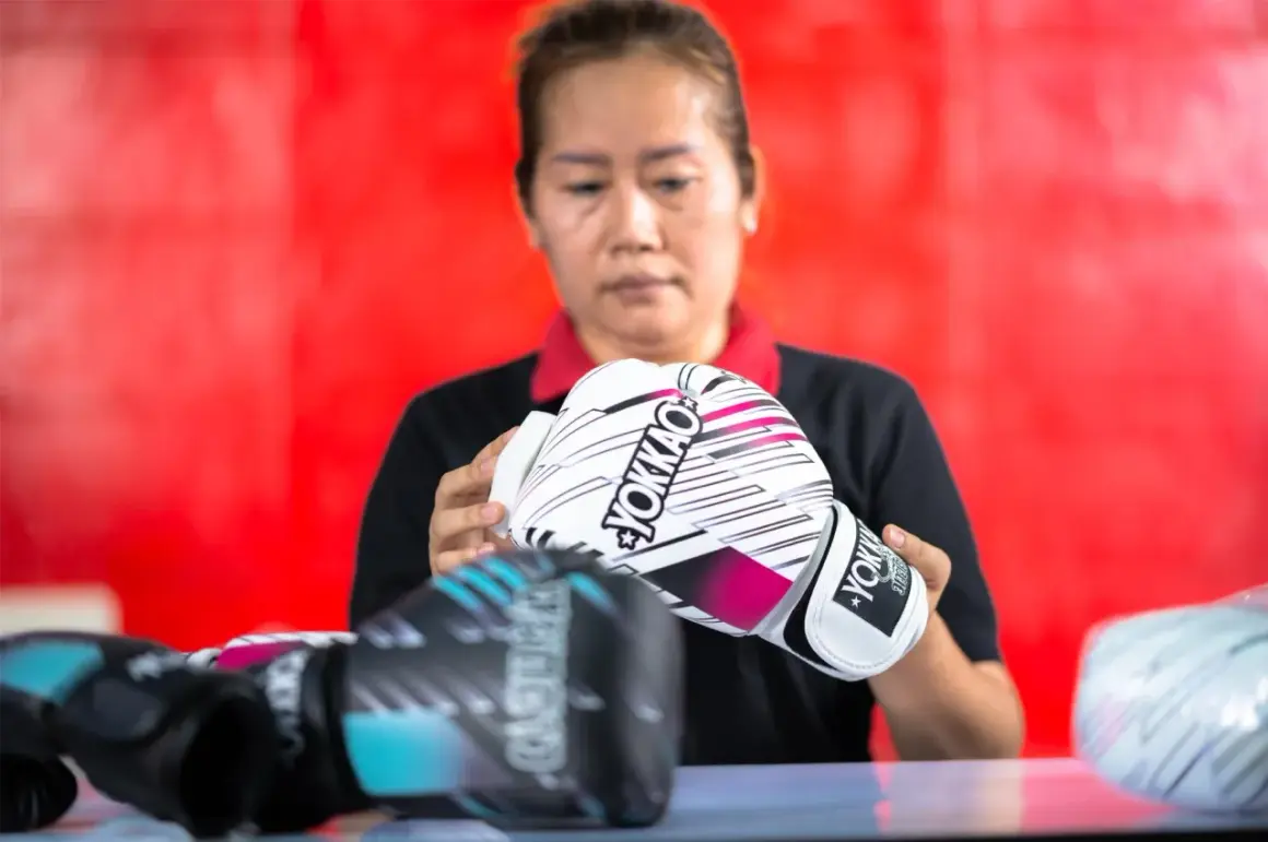 A woman inspects a pair of white YOKKAO sparring gloves. Other gloves, possibly bag gloves, are visible in the foreground.