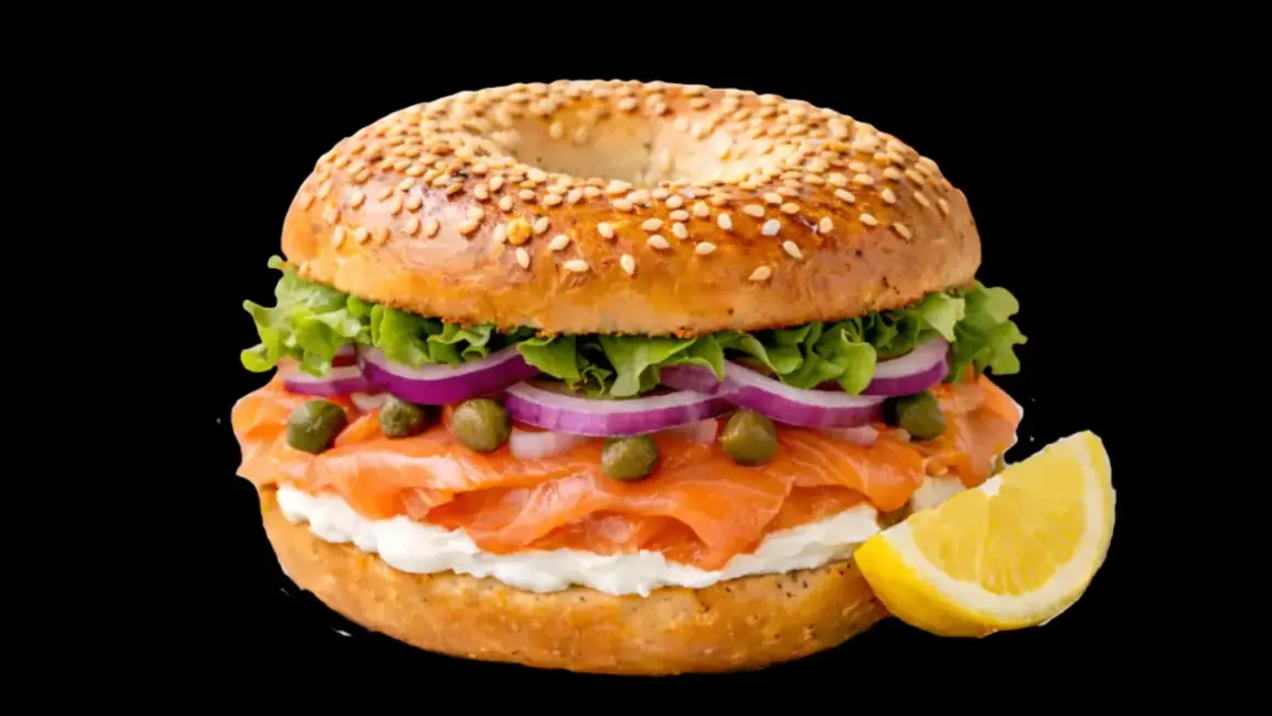 Un délicieux bagel saumon garni de fromage frais, oignons rouges, câpres et laitue, avec un quartier de citron à côté.