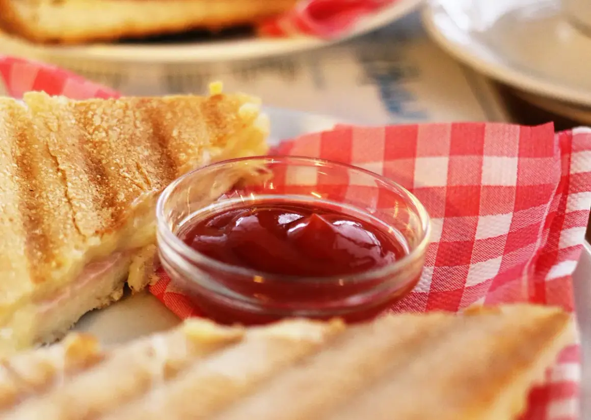 Un sándwich a la parrilla con una pequeña taza de ketchup. ¿El ketchup es dulce o salado?