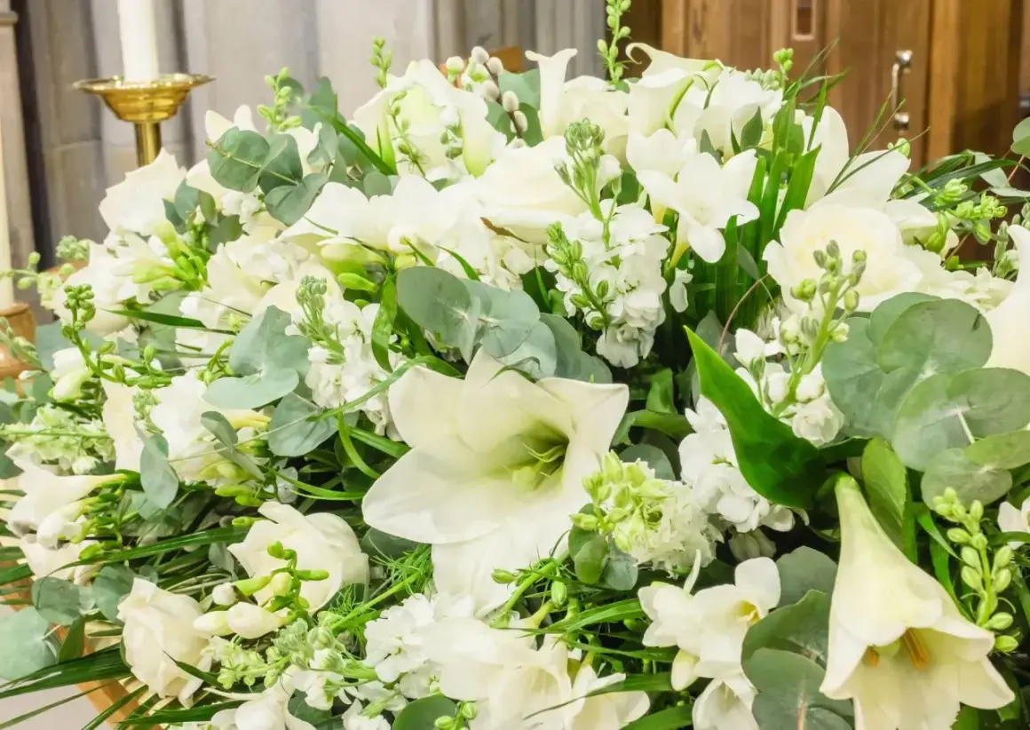 Białe lilie i inne kwiaty tworzą elegancki bukiet, idealny jako wyraz pamięci i szacunku.