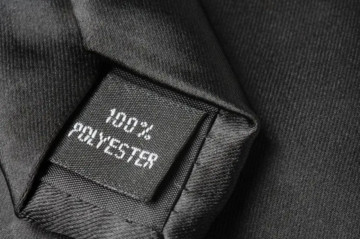 Czarna metka z napisem "100% POLYESTER" na tle eleganckiej tkaniny. Czy poliester się rozciąga? Ten materiał wygląda na wytrzymały.
