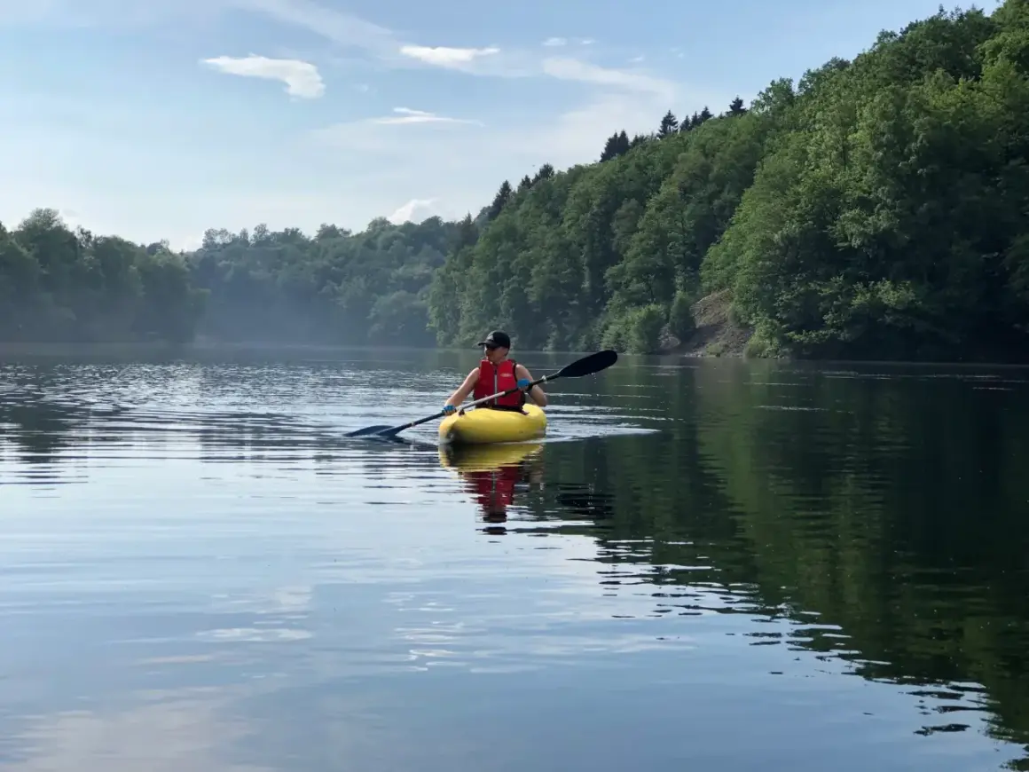 Person in gelbem Kajak genießt eine friedliche Kanu fahrt auf einem ruhigen See, umgeben von üppigen grünen Wäldern.