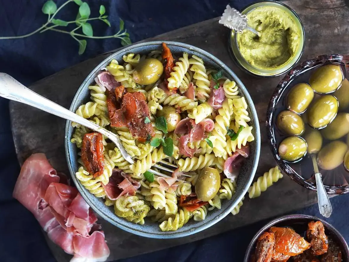 Pasta salad with pesto, sun-dried tomatoes, olives, and prosciutto.