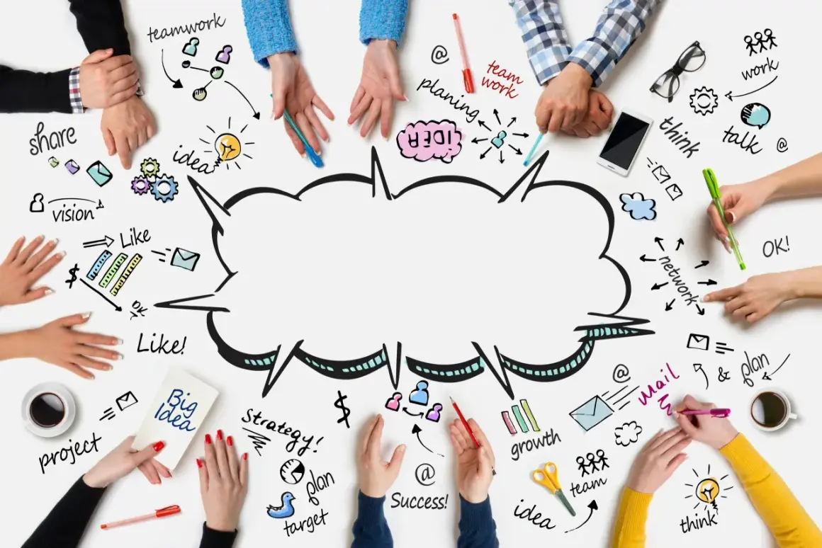 Ludzie tworzą burzę mózgu, rysując na stole schematy: teamwork, idea, plan, vision, share, growth, success.