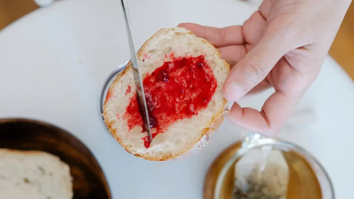 Ein Stück Brot wird mit Marmelade bestrichen, ein Genuss, der die Bedeutung eines Cheat Days unterstreicht.