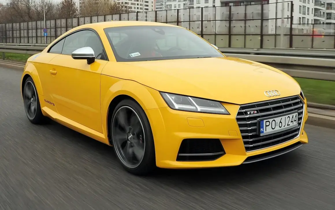 Żółte Audi TT RS, jedna z nowszych audi tt generacji, pędzi po drodze.