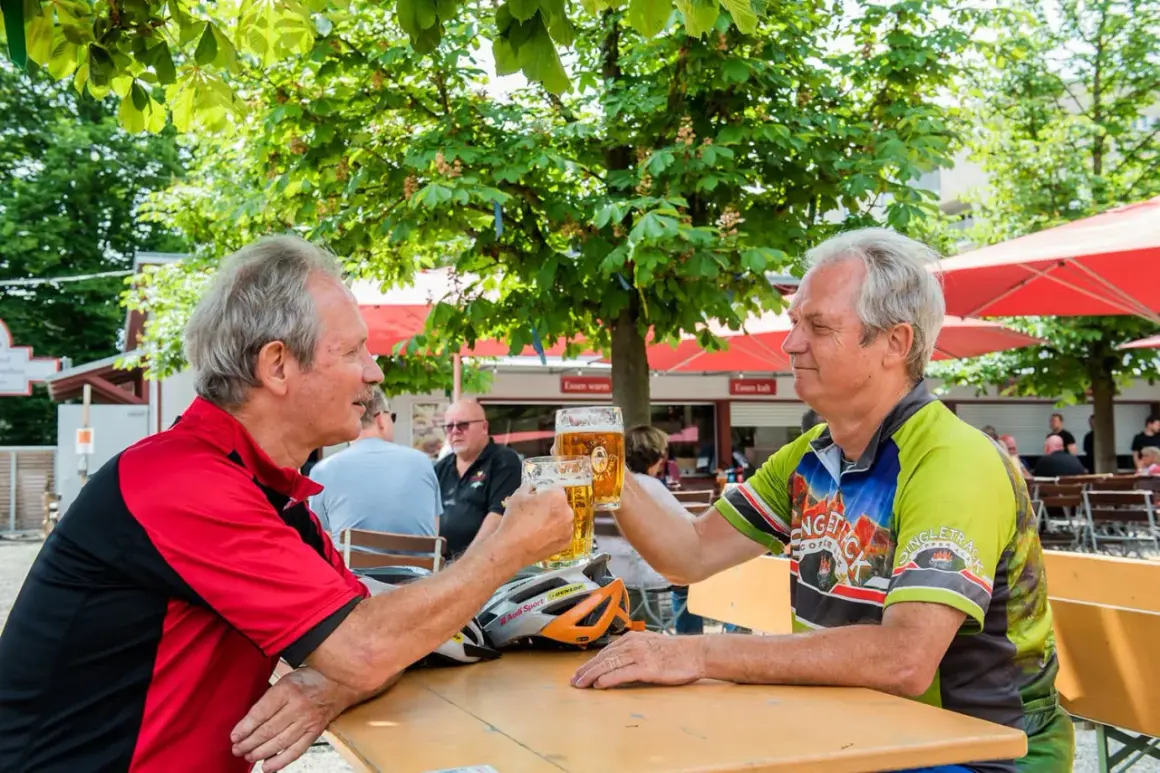 Zwei Radfahrer stoßen im Stadtbiergarten Schorndorf mit Bier an.