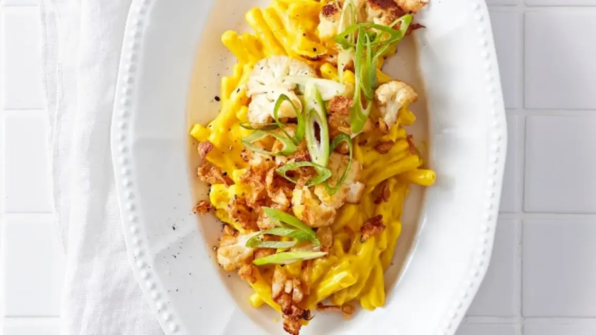 Cremiges Blumenkohl Mac and Cheese mit knusprigen Zwiebeln und Frühlingszwiebeln garniert.