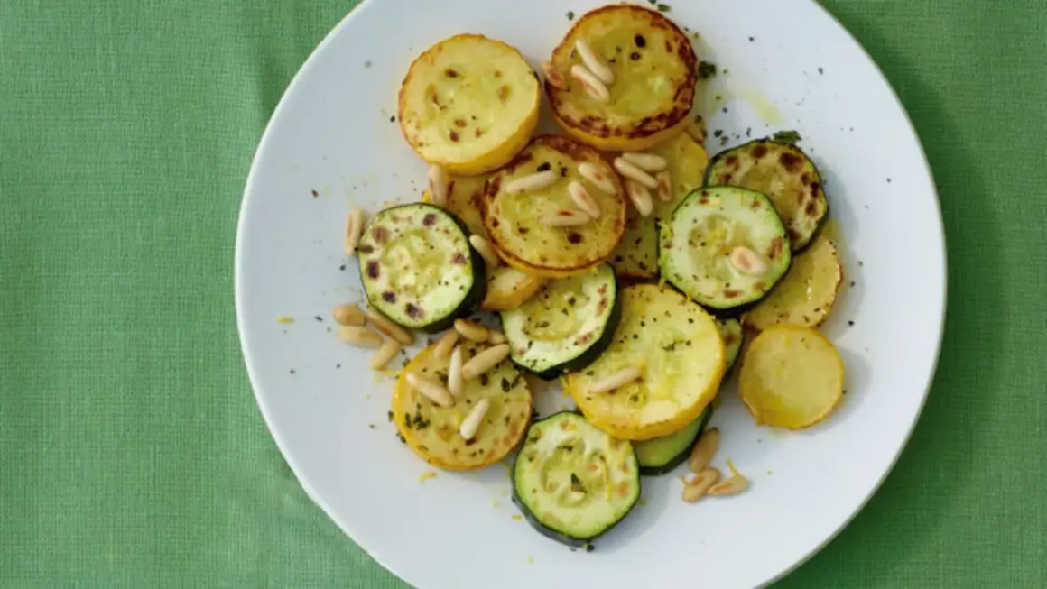 Zucchini gebraten italienisch mit Pinienkernen auf einem weißen Teller. Ein köstliches Gericht, das an einen sonnigen Tag in Italien erinnert.