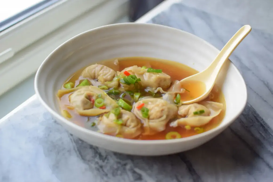 Aksamitna zupa wonton z kawałkami chili i szczypiorku, gotowa do nabrania łyżką.