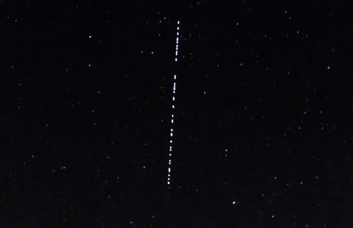 Nocne niebo z gwiazdami i pionowym sznurkiem jasnych punktów, przypominających przeloty Starlink.