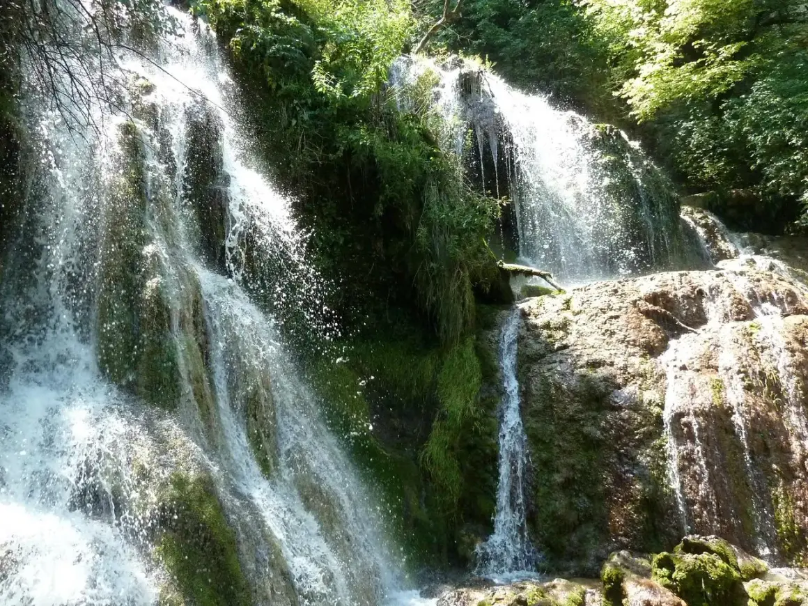 Cascada exuberante, ideal para saber qué visitar en Bulgaria. El agua cae sobre rocas cubiertas de musgo y vegetación frondosa.