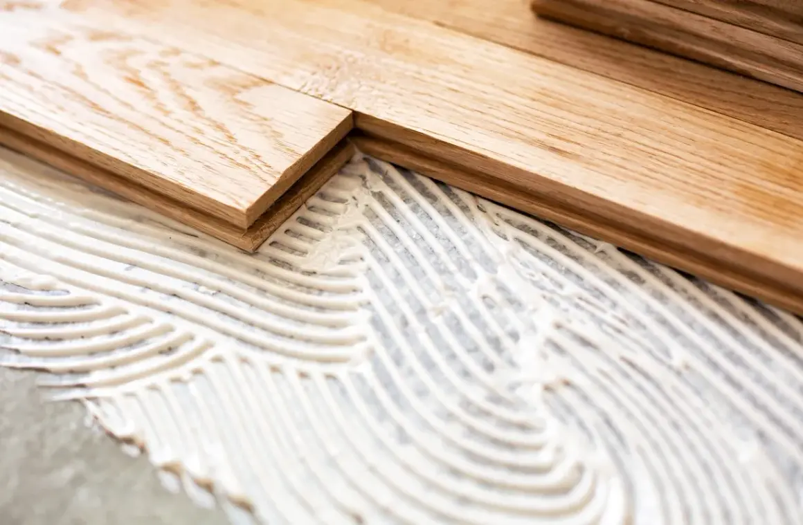 Pose de parquet en bois sur du béton avec de la colle. Les lames de bois sont prêtes à être fixées.