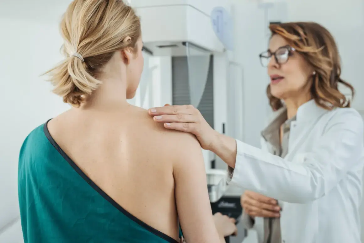 Ärztin legt Hand auf Schulter einer Patientin während einer Mammographie mit Implantaten.