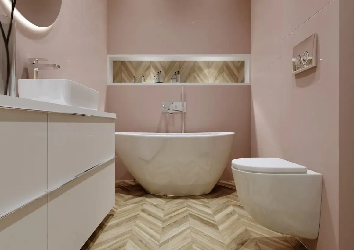 Elegancka łazienka z wolnostojącą wanną i baterią wannową. Jasnoróżowe ściany, drewniana podłoga w jodełkę.