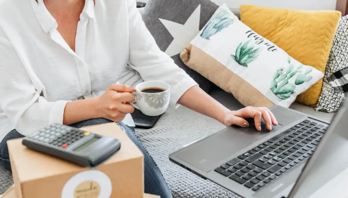 Kobieta z kawą uczy się, jak sprzedawać na OLX, korzystając z laptopa i kalkulatora.