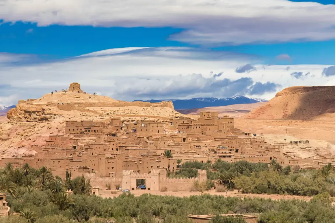 Ait Ben Haddou, en historisk befäst stad i Marocko, reser sig mot en blå himmel med moln.