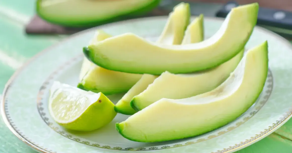 Plasterki awokado i ćwiartka limonki na talerzu. Awokado właściwości zdrowotne czynią je idealnym składnikiem sałatek i tostów.